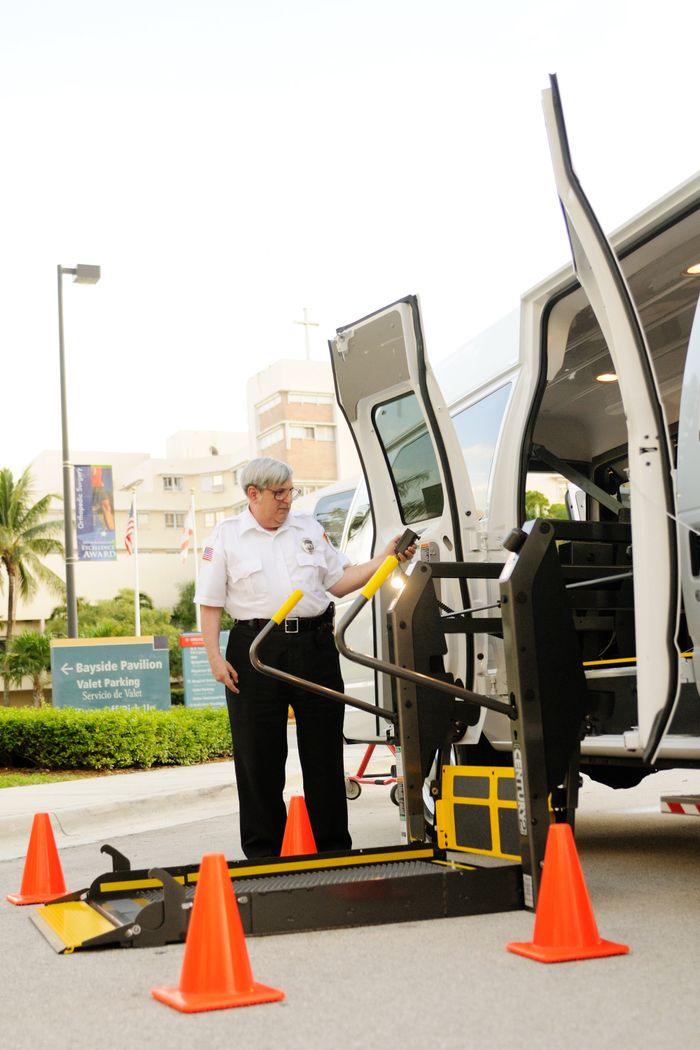 Safety officer demonstrating the use of a wheelchair lift in a van at a facility.